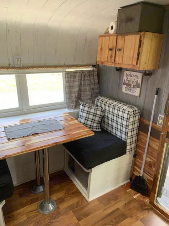 Inviting rv rental interior. Features a cozy plaid bench, wooden table, storage, and homey camp decor.. Nomad Rear fold 1962