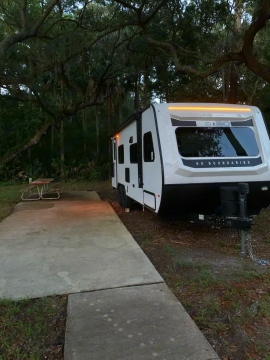 RV rental with lights on, parked at a wooded campground site beside a picnic table.. Forest River no boundaries 2020