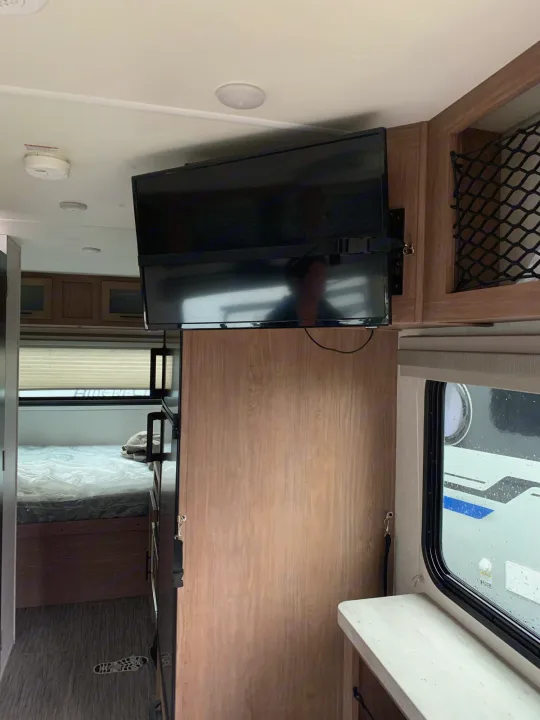 This rv rental offers a compact interior with a wall-mounted TV, a bed, and a window showing another vehicle outside.. Forest River no boundaries 2020