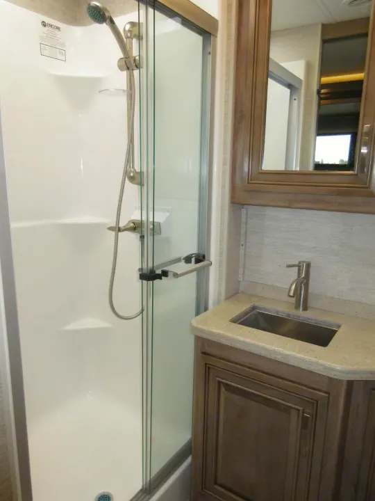 Compact RV rental bathroom showcasing a clean white shower with glass door and a sleek vanity with sink.. Jayco Seneca 2021