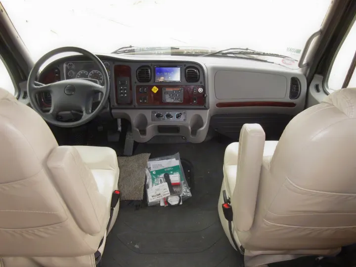 Inside an RV rental, showing the clean and well-equipped front cabin with dashboard, steering wheel, and beige leather seats.. Jayco Seneca 2021
