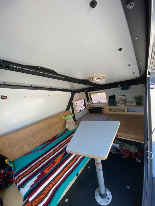 Explore this cozy RV rental interior with a bench, table, bed, Grogu, and ample storage for your next adventure.. TAXA Outdoors Tigermoth Camper 2021