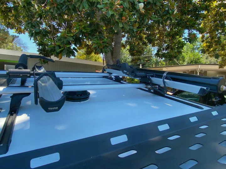 View of a white RV rental's roof, featuring a Thule kayak carrier, crossbars, and a mounted storage tube.. TAXA Outdoors Tigermoth Camper 2021