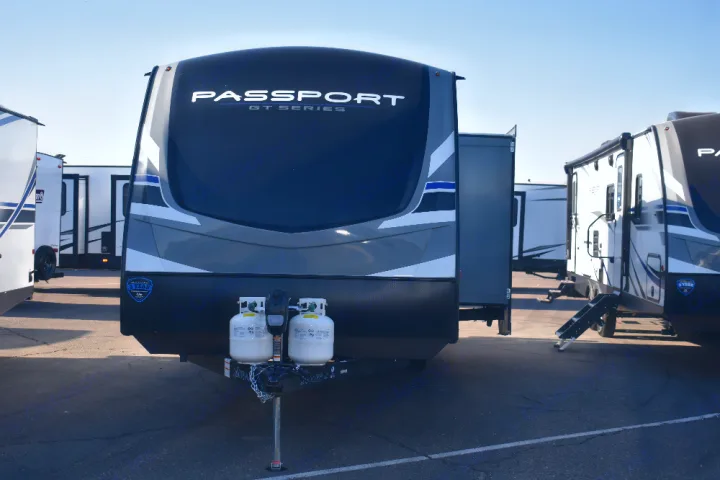 Front of a Passport GT Series travel trailer with propane tanks, ideal for an rv rental. Parked on asphalt under a clear sky.. Keystone Passport 2021
