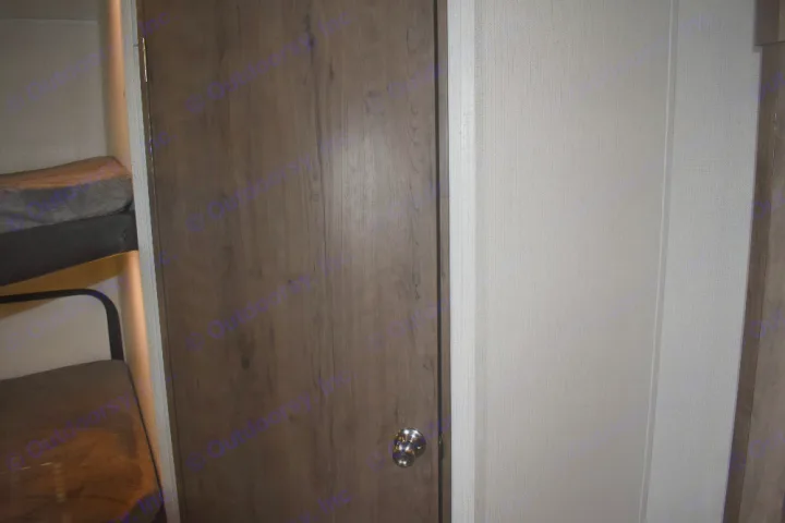 Inside an RV rental, showing a dark wood door with metallic knob, textured light walls, and bunk beds with a soft blanket.. Keystone Passport 2021
