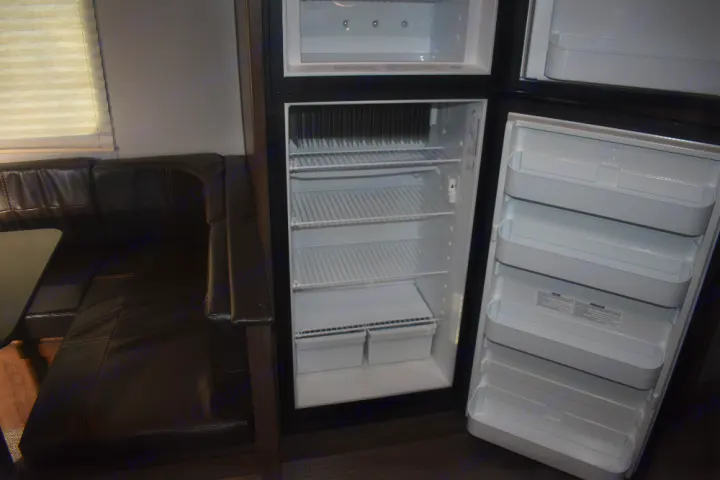 RV rental interior: Open refrigerator and dark leather dinette, showcasing a functional kitchen space.. Keystone Passport 2021