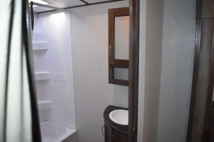 This RV rental bathroom features a compact white shower/tub, vanity with sink, and medicine cabinet for comfortable travel.. Keystone Passport 2021