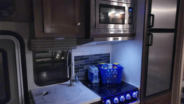 RV rental kitchen: A compact galley with stainless microwave, stove (blue lights on knobs), sink, and fridge. Fully equipped.. Forest River Sunseeker 2019