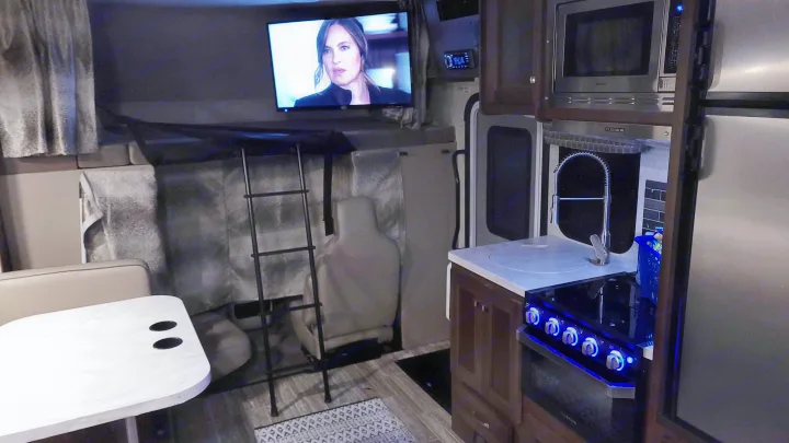Explore this RV rental's interior: kitchen with stove/sink, dining table, TV, and ladder to the upper bunk.. Forest River Sunseeker 2019
