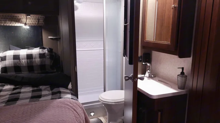 This RV rental features a cozy bedroom with plaid bedding, plus a compact bathroom with a toilet, shower, and sink setup.. Forest River Sunseeker 2019