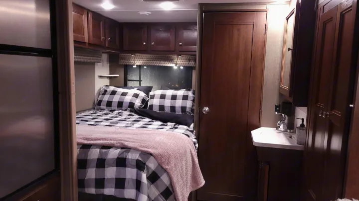This cozy RV rental features a compact bedroom with buffalo check bedding, an integrated bathroom sink, and storage cabinets.. Forest River Sunseeker 2019