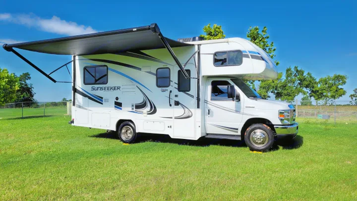 This white Sunseeker RV rental, with its awning extended, sits on green grass under a clear blue sky.. Forest River Sunseeker 2019