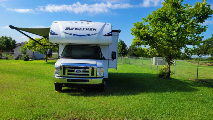 This RV rental, a white Sunseeker, is parked on lush green grass with its awning extended under a bright sky.. Forest River Sunseeker 2019
