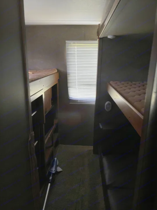 RV rental interior: A narrow aisle flanked by two bunk beds with mattresses. A window with blinds illuminates this compact sleeping area.. Keystone Summerland 2017