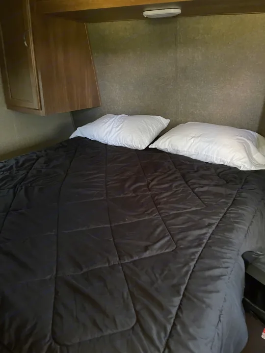 Comfortable bed in an RV rental with a black comforter and white pillows, perfect for a cozy night's stay.. Keystone Summerland 2017