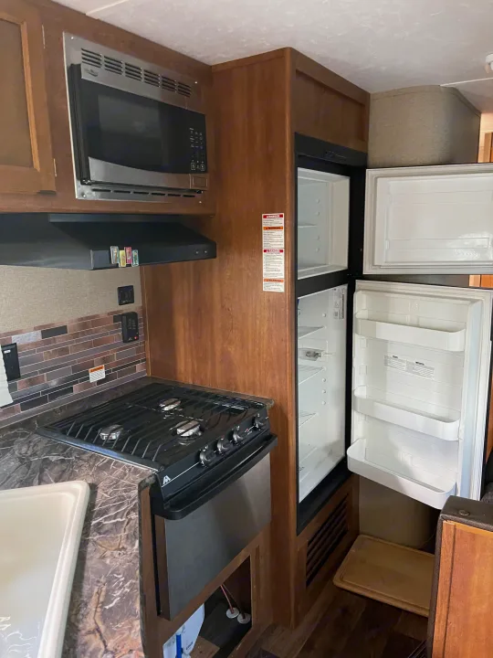 Inside this RV rental's kitchen: a microwave, gas stove, and open refrigerator are ready for your culinary journeys.. Keystone Summerland 2017