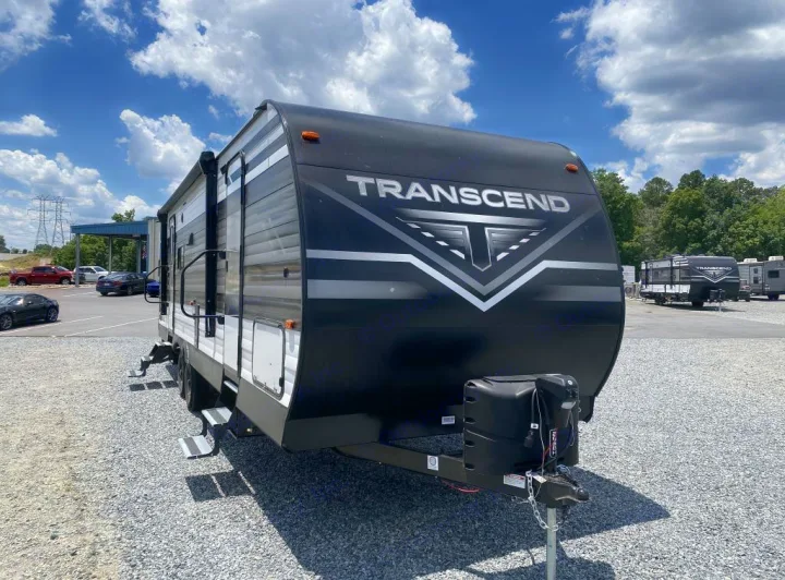 A sleek black and white Transcend travel trailer is ready for your next rv rental adventure, parked on a gravel lot.. Grand Design Transcend Xplor 2021