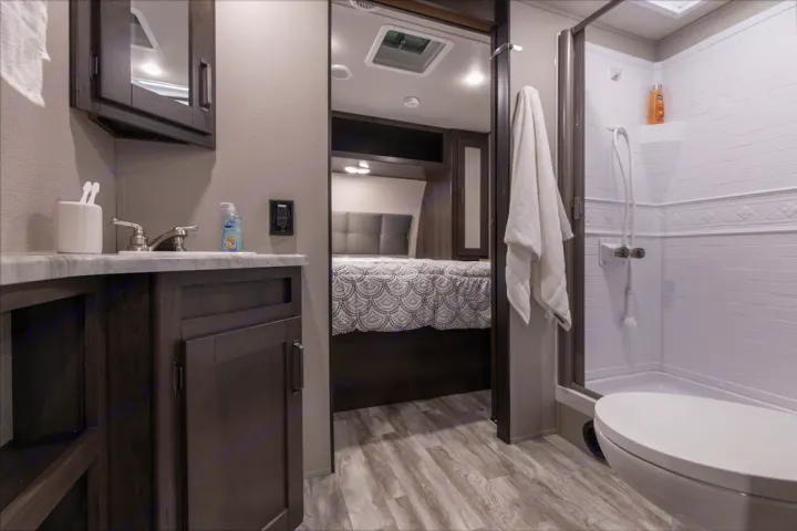 RV rental interior: a practical bathroom with sink, shower, and toilet, next to a comfortable bedroom space.. Grand Design Transcend Xplor 2021