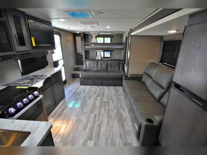 Explore this modern RV rental interior featuring a kitchen, living area with sofas, and bunk beds, designed for comfortable travel.. Grand Design Transcend Xplor 2021