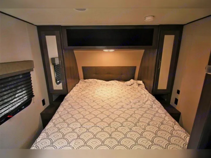 RV rental bedroom with a comfortable bed, dark wood overhead & side storage cabinets, and a window for a cozy stay.. Grand Design Transcend Xplor 2021