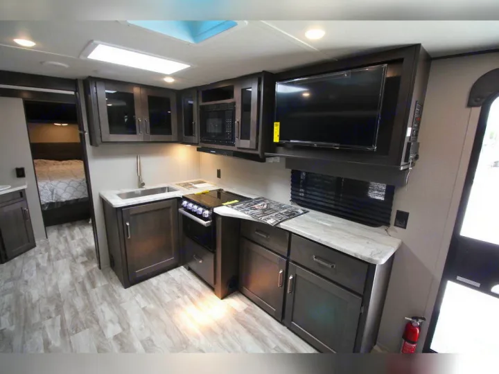 Inside this RV rental: a well-equipped kitchen area with TV, plus a glimpse into the comfortable bedroom.. Grand Design Transcend Xplor 2021