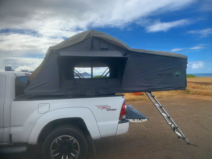 White Toyota Tacoma with a Nomadic rooftop tent open, ideal for an RV rental adventure. Ladder extends to ground with coastal view.. Toyota Tacoma 2009