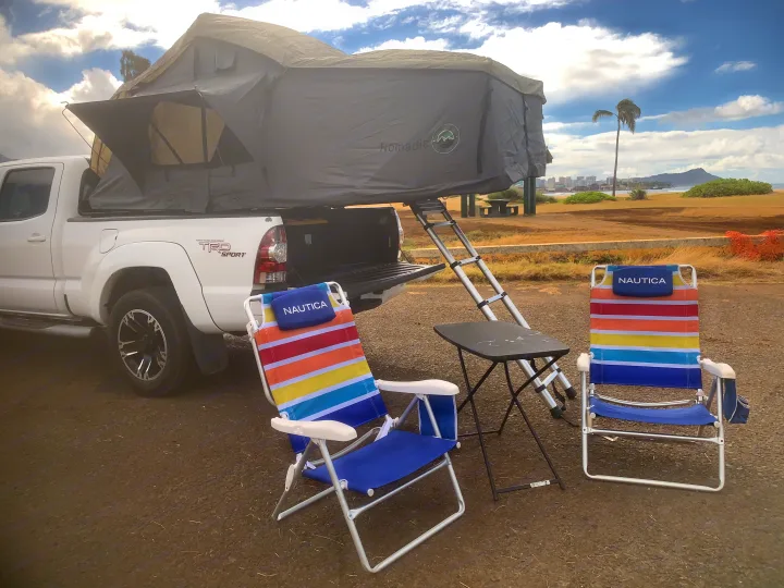 White Toyota pickup with a Nomadic rooftop tent, chairs, and table by the coast. Experience the outdoors with an rv rental adventure!. Toyota Tacoma 2009