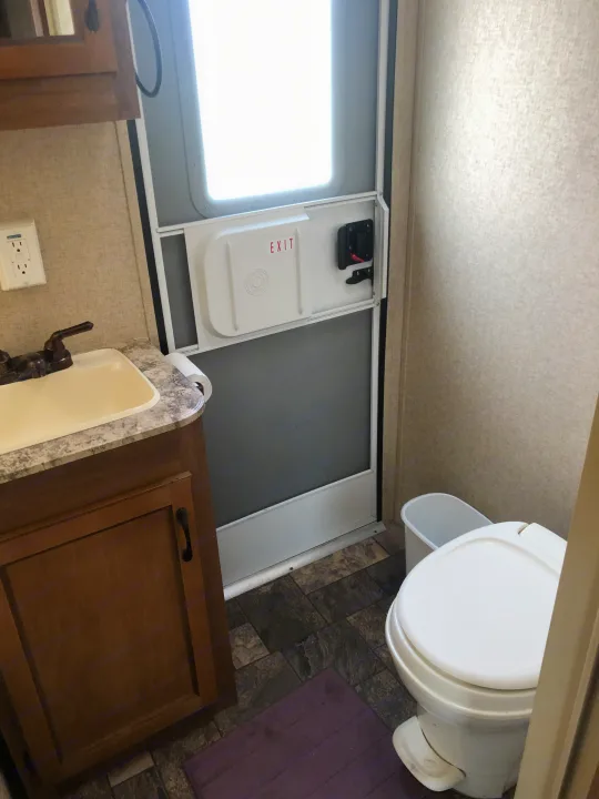 Inside an RV rental, a compact bathroom features a sink, toilet, and the main exit door with an 'EXIT' sign for clarity.. Forest River Coachmen Catalina 2016