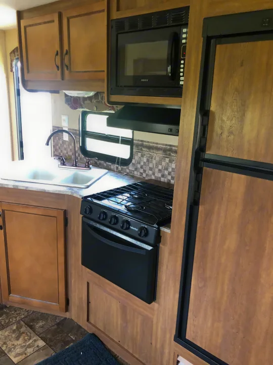 Explore the functional kitchen of this RV rental, featuring light wood cabinets, a sink, microwave, stove, and integrated refrigerator.. Forest River Coachmen Catalina 2016