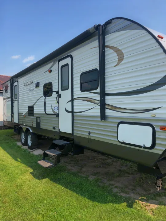 Side view of a white and olive green Catalina Coachmen travel trailer, ideal for an RV rental. Features steps & awning.. Forest River Coachmen Catalina 2016