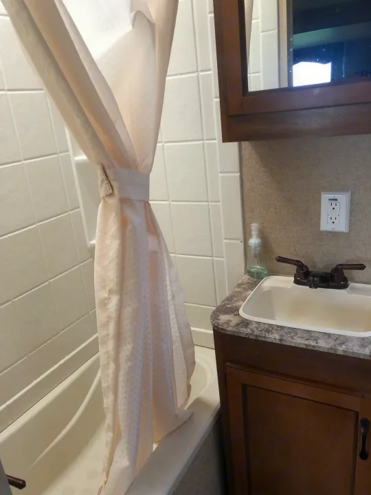RV rental bathroom with a white tiled shower/tub, a tied curtain, and a vanity featuring a sink and dark faucet.. Forest River Coachmen Catalina 2016