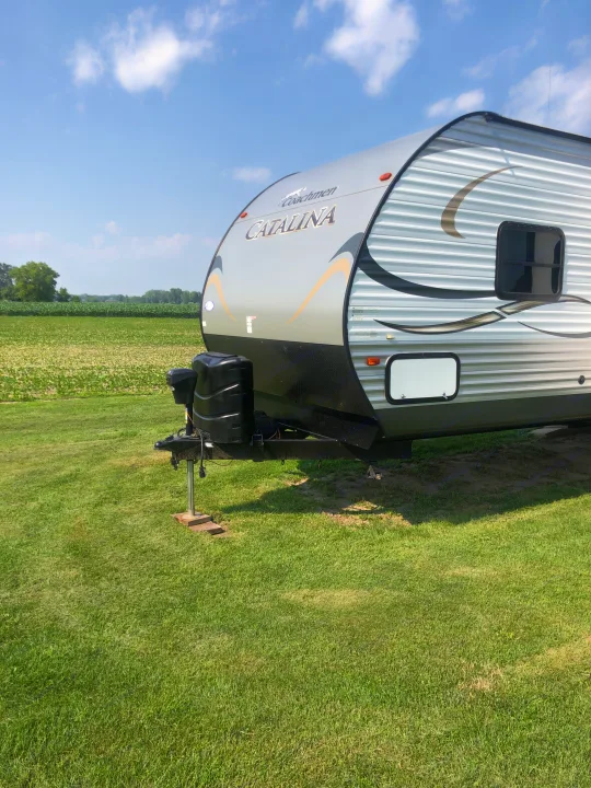 Front view of a Coachmen Catalina RV rental parked on vibrant green grass next to a crop field under a blue sky.. Forest River Coachmen Catalina 2016