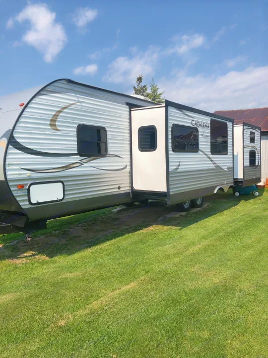 Spacious Catalina travel trailer RV rental, with an extended slide-out, parked on green grass under a partly cloudy sky.. Forest River Coachmen Catalina 2016