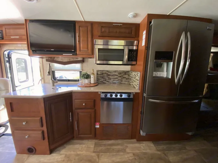 This RV rental kitchen features a stainless steel fridge, microwave, cooktop, sink, TV, and wood cabinetry.. Forest River Georgetown 2015
