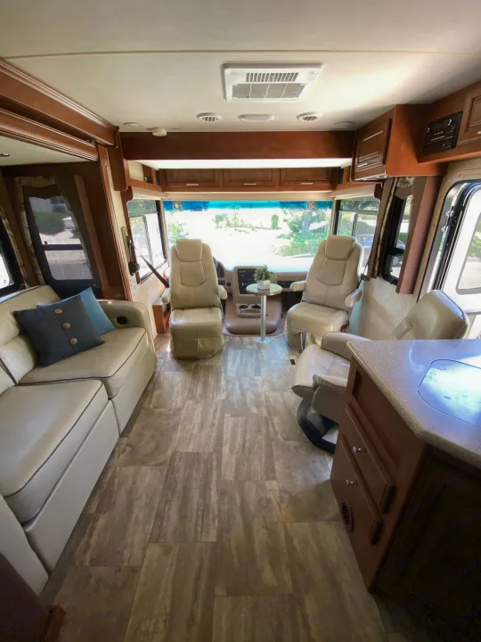 Bright RV rental interior: cream sofa, captain's chairs, wood accents, and large windows. Spacious motorhome living area.. Forest River Georgetown 2015