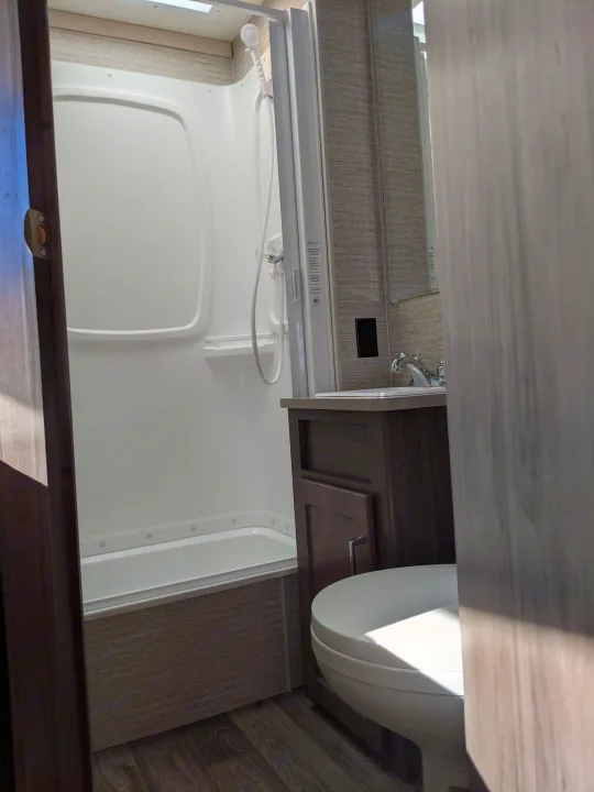 RV rental bathroom with a white shower/tub combo, sink vanity, and toilet.. Winnebago Minnie Winnie 2022
