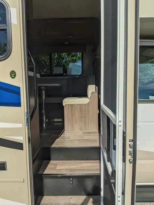 RV rental interior: Steps from the open entry door lead to a dining booth, table, and window overlooking trees.. Winnebago Minnie Winnie 2022