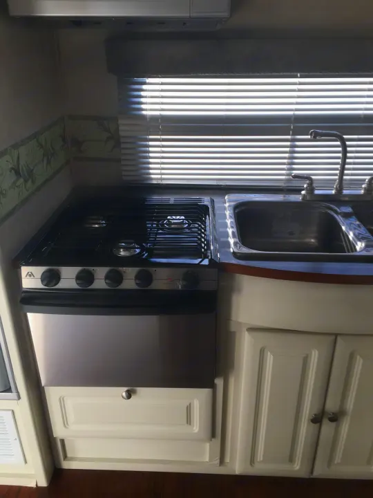 RV rental interior showing a clean, compact kitchen with a stainless steel gas stove/oven, double sink, and window blinds.. Max Lite ML26RK 2006