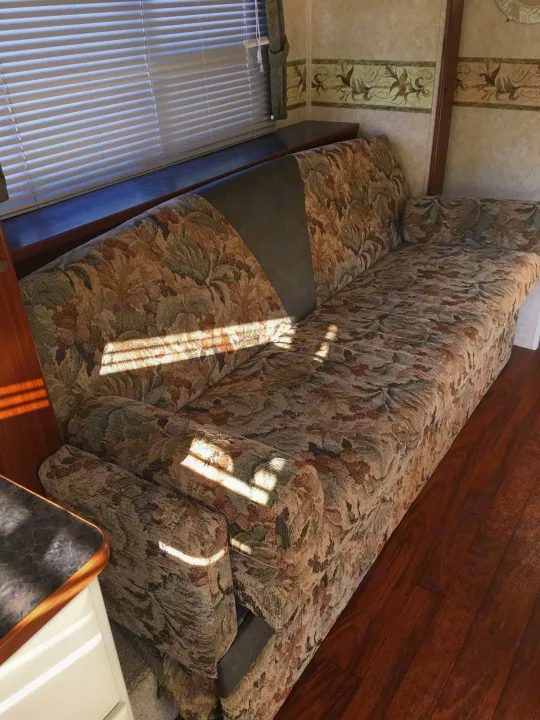 Interior of an RV rental showing a floral sofa, window blinds, and hardwood floor, with sunbeams across the couch.. Max Lite ML26RK 2006