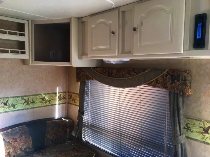 Inside an RV rental: white overhead cabinets, a stereo, comfy seating, and a window with blinds.. Max Lite ML26RK 2006
