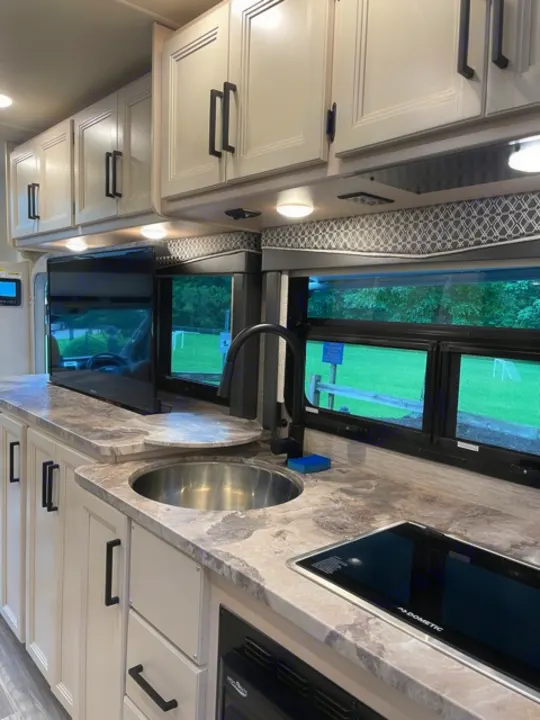 RV rental's bright interior kitchen: light cabinets, black hardware, stainless sink, and Dometic glass stovetop.. Thor Gemini 2021