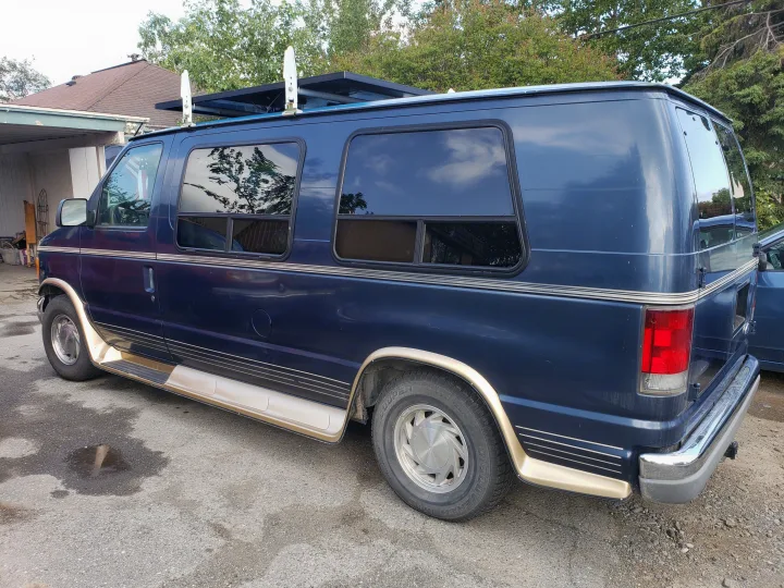 Dark blue conversion van, equipped with a roof rack and side steps, shown parked. Could be used as an RV rental.. Ford Econoline Club Wagon 1998