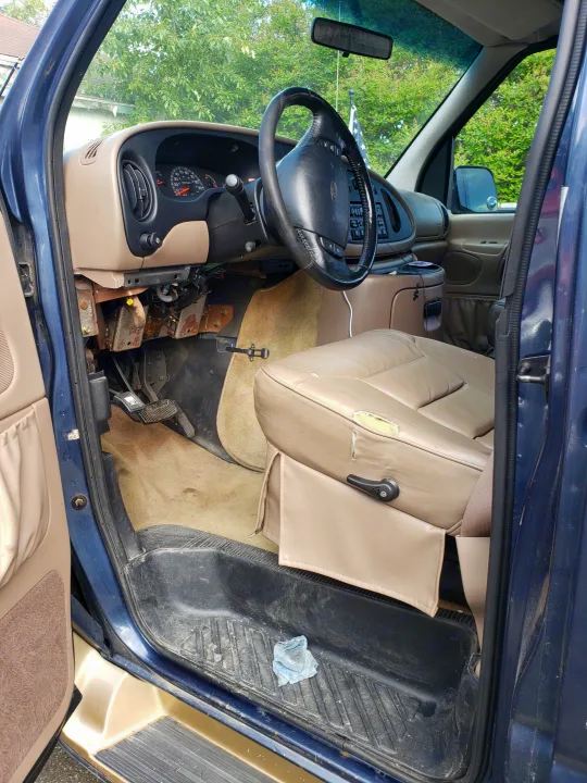 RV rental van interior: driver's seat (torn), exposed dash wiring, steering wheel, and dirty floor mats.. Ford Econoline Club Wagon 1998