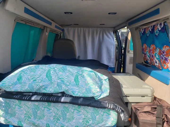 RV rental van interior: tropical bed, privacy curtain, and cooler for a comfortable mobile living.. Ford Econoline Club Wagon 1998
