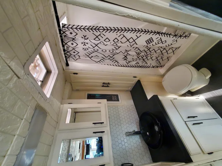 Compact rv rental bathroom: geometric shower curtain, white toilet, black sink vanity, and hexagonal wall tile.. Safari Trek 2610 1994