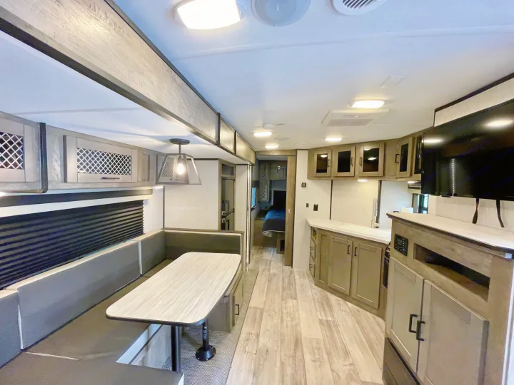 Spacious RV rental interior with a modern dining booth, kitchen area, and private bedroom access, perfect for travel.. Heartland North Trail 2021