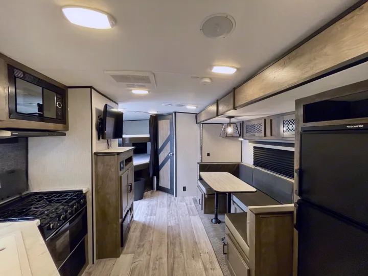 Inside an RV rental: modern kitchen with microwave & stove, comfy dinette, and bunk beds visible for spacious living.. Heartland North Trail 2021