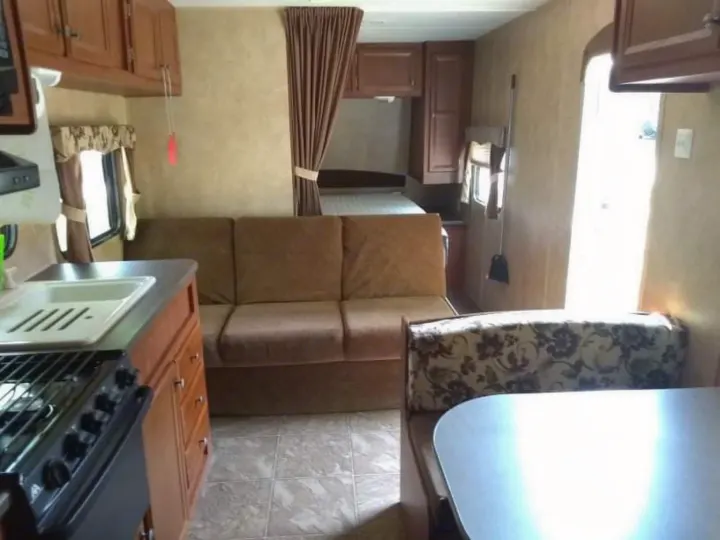 RV rental interior showing kitchen, brown sofa, patterned dining booth, and a rear sleeping area with privacy curtain.. Jayco Jay Flight Swift 2012
