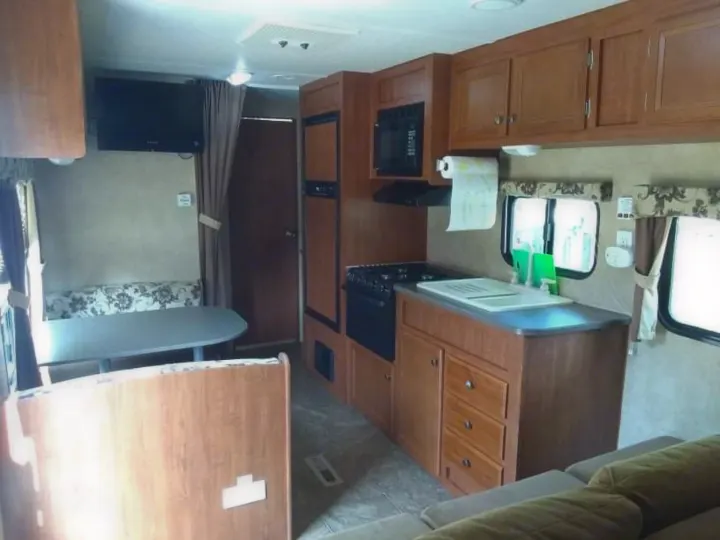 Interior of an RV rental: full kitchen, dinette, TV, and living space. Wood cabinets, light walls, and tiled floor.. Jayco Jay Flight Swift 2012