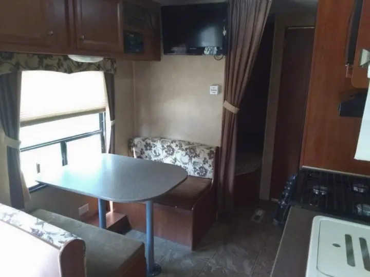 An RV rental interior featuring a comfortable dinette with patterned cushions, a wall-mounted TV, and kitchen amenities.. Jayco Jay Flight Swift 2012